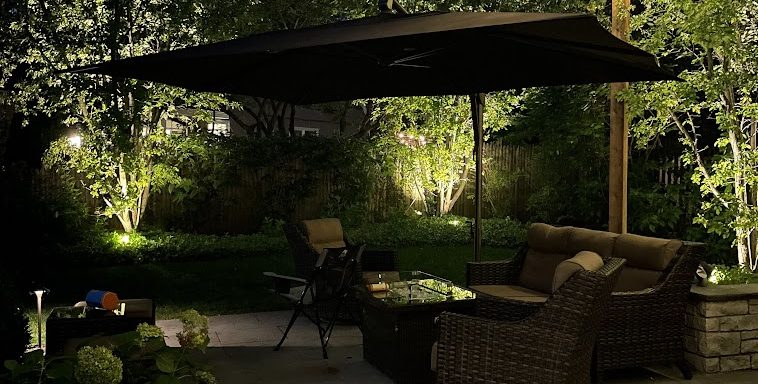 Landscape Lighting Installation in Hartland, WI Custom outdoor lighting design highlighting a backyard patio with string lights, garden accents, and outdoor seating for nighttime entertaining in Lake Geneva, Wisconsin.